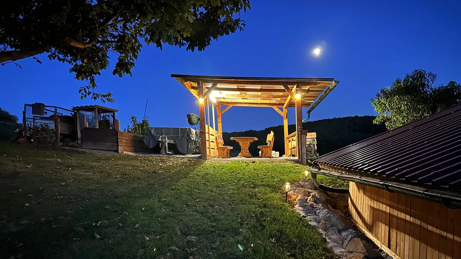 Beleuchtete Holzlaube am Abend, darüber der Mond