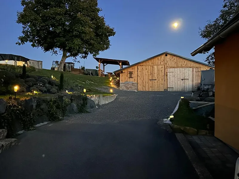 Zufahrt am Abend mit Gartenlichtern, Holzschuppen und Mond