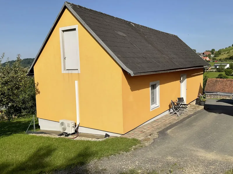 Gartenseite des gelben Ferienhauses mit Bistrotisch auf der Terrasse