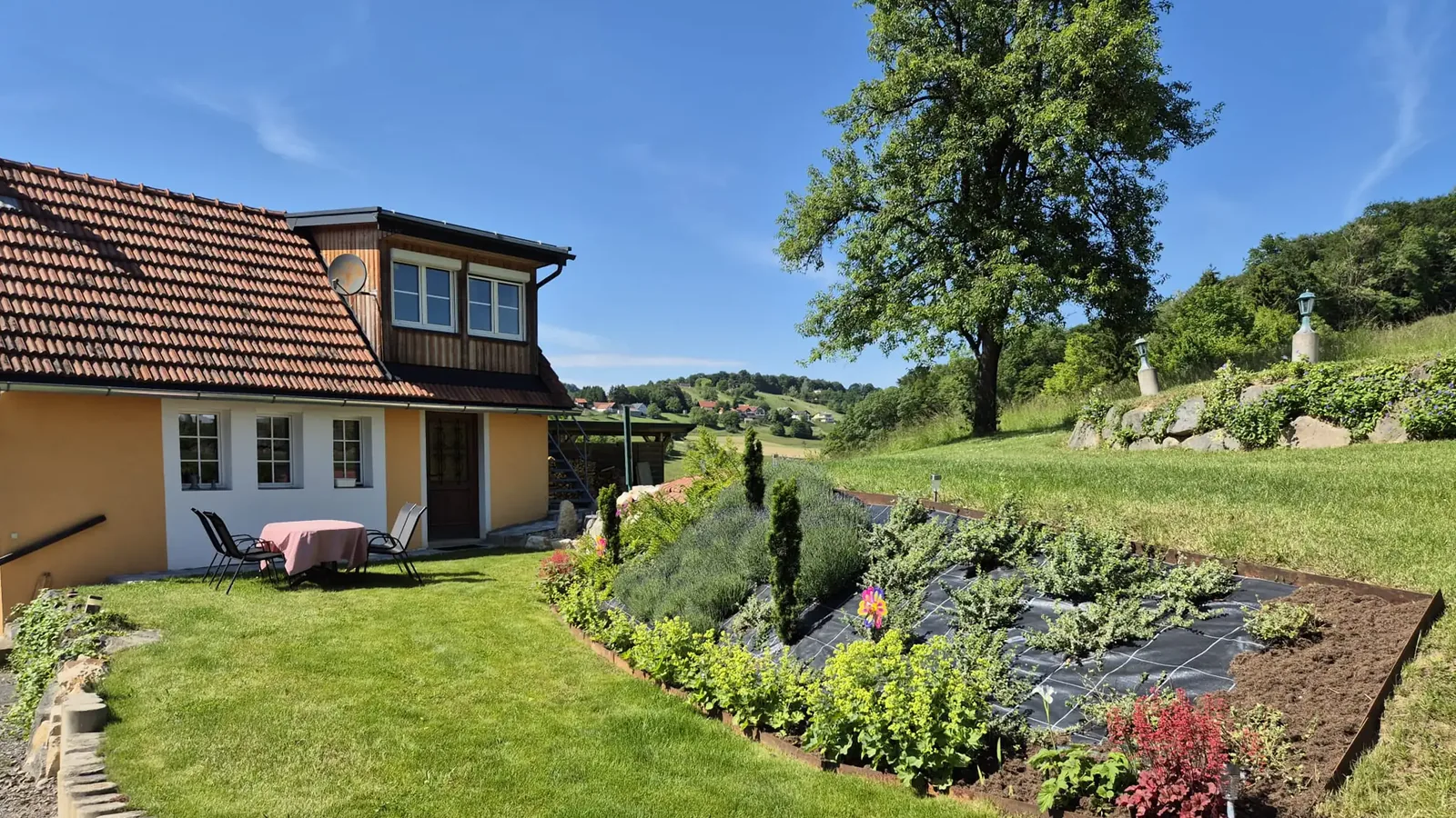 Garten am Hang mit Beeten, Sitzplatz auf der Wiese und großem Baum