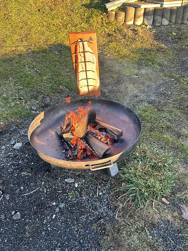 Feuerschale mit brennendem Holz, daneben gart ein Fisch am Brett